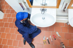 Plumber with cap repairing sink in public bathroom